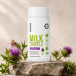 A bottle of Uvora Milk Thistle supplements rests on a rock next to fresh milk thistle plants.